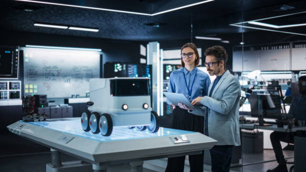 istock Portrait of Two Colleagues Working in a Research Facility, Using Laptop Computer to Develop a Futuristic Robot for Autonomous Deliveries. Manufacturing Specialist Doing a Demonstration to Team Manager 2187842948