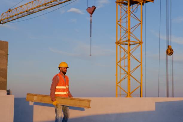 istock Construction worker carrying wooden plank on rooftop at sunset 2187850767
