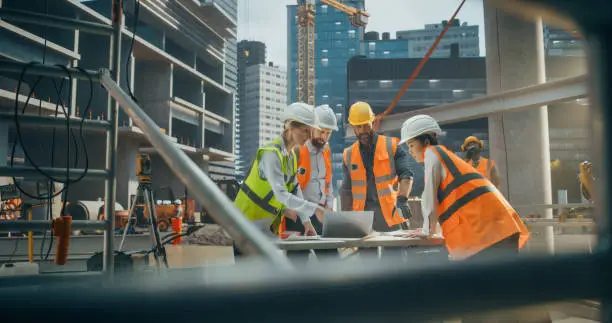 Female Civil Engineer Using a Laptop Computer and Talking with General Workers at a Residential Building Construction Area. Female and Male Employees Oversee the Real Estate Project Plan Female Civil Engineer Using a Laptop Computer and Talking with General Workers at a Residential Building Construction Area. Female and Male Employees Oversee the Real Estate Project Plan