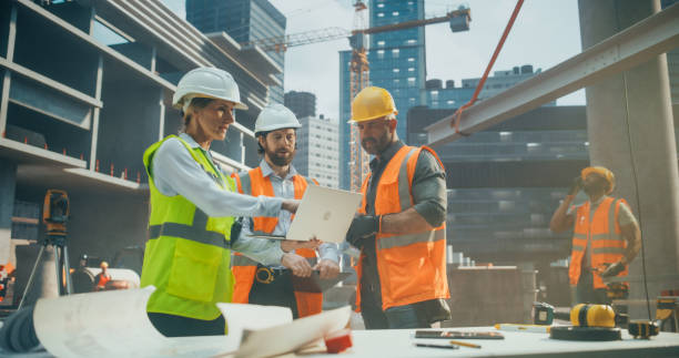 istock Crew of Construction and Site Managers Having a Meeting at a Construction Site with Skeleton Frame Building with Concrete and Steel Beams. Industrial Specialists Using Laptop to Check the Blueprints 2187852681