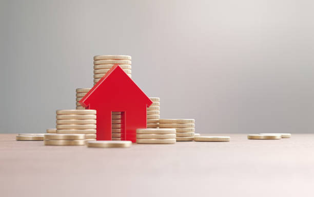istock Red House Symbol And Gold Colored Coin Stacks Before Defocused Background 2187860341
