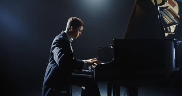 istock Young Pianist Playing Academic Music, Performing Classical Solo Compositions on a Dark Stage. Grand Piano Resounds With Rich, Melodic Tones of a Romantic Ballad. Pianist Playing Under a Spotlight 2187864339