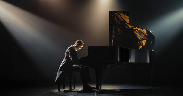 istock Young Pianist Playing Academic Music, Performing Classical Solo Compositions on a Dark Stage. Grand Piano Resounds With Rich, Melodic Tones of a Romantic Ballad. Pianist Playing Under a Spotlight 2187864894