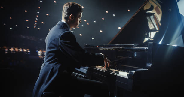 istock Male Pianist Sits at Black Grand Piano, Playing a Mesmerizing Classical Sonata. Audience Watching the Musician Play on Stage. Artist is Focused on Creating Beautiful Instrumental Ballad 2187865059