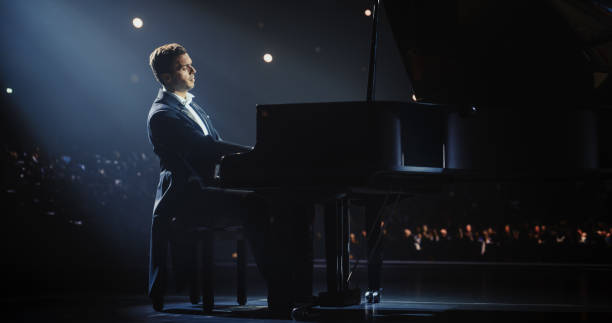 istock Classical Piano Concert: Under the Spotlight, Pianist Delivering a Powerful Performance on the Grand Piano. Elegant Stage Setting Complements His Passionate Playing, Leaving the Audience Happy 2187865365