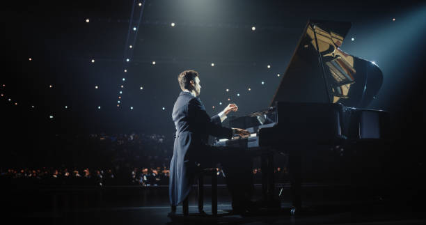 istock Male Pianist Sits at Black Grand Piano, Playing a Mesmerizing Classical Sonata. Audience Watching the Musician Play on Stage. Artist is Focused on Creating Beautiful Instrumental Ballad 2187865796
