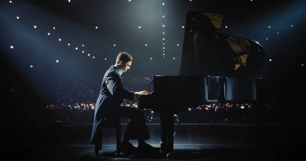 istock Classical Piano Concert: Under the Spotlight, Pianist Delivering a Powerful Performance on the Grand Piano. Elegant Stage Setting Complements His Passionate Playing, Leaving the Audience Happy 2187865863