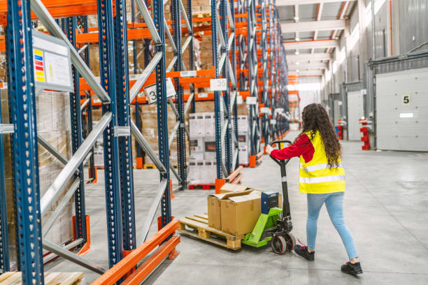 istock Warehouse worker moving boxes with pallet jack in logistics center 2187866139