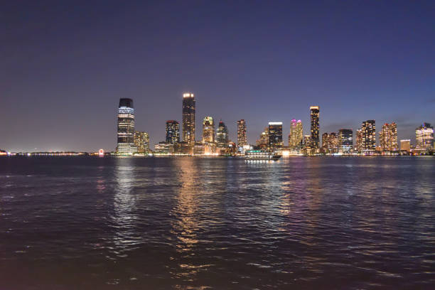 A city skyline is reflected in the water at night. The water is calm and the city lights are shining brightly