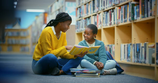 istock Library, girl and educator reading book for education, learning and knowledge for storytelling and language. Teacher, black woman and kid on floor for fun, fantasy stories and development or relaxing 2187876907
