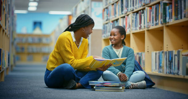 istock Library, girl and teacher reading book for education, learning and knowledge for storytelling and language. Educator, black woman and kid on floor for fun, fantasy stories and development or relaxing 2187876909
