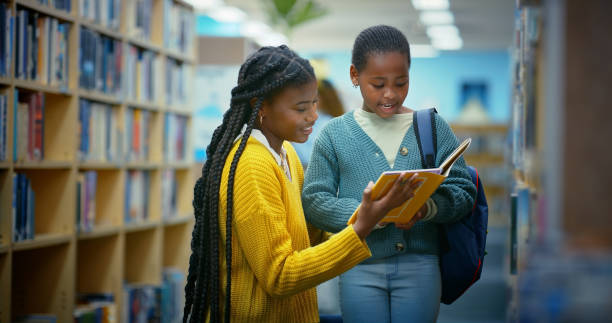 istock Library, child and black woman help reading book for education, learning and knowledge for storytelling and language. Educator, teacher and girl for fun, fantasy stories and development or relaxing 2187876948