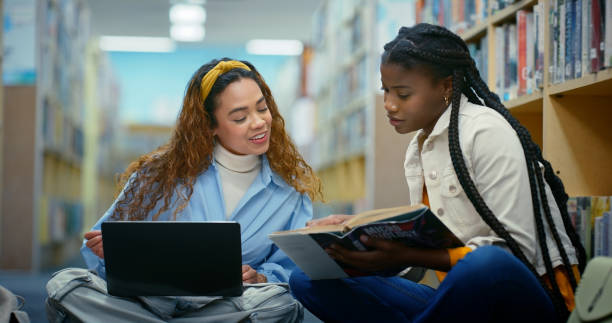 istock University, students and women in library, laptop and teamwork for assignment, learning and internet. People, college and friends on floor, pc and scholarship with books, technology and education 2187876991