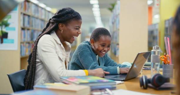 istock Teacher, child and laptop for education in library with elearning support, information and advice. Woman, student and online research with studying, assessment and scholarship application for tuition 2187877062