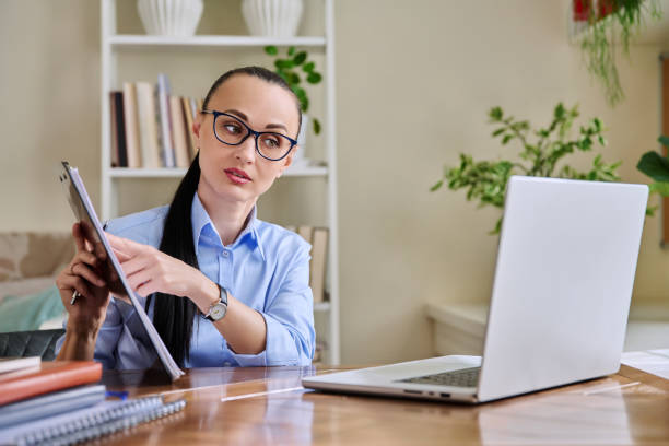 istock Business woman with clipboard sitting at workplace, looking talking at computer screen 2187885238
