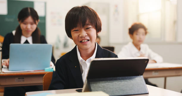 istock Boy, child and happy in classroom with tablet, portrait and excited for e learning, development and progress. Learner, school kids and touchscreen for education, smile and study at academy in Japan 2187885860