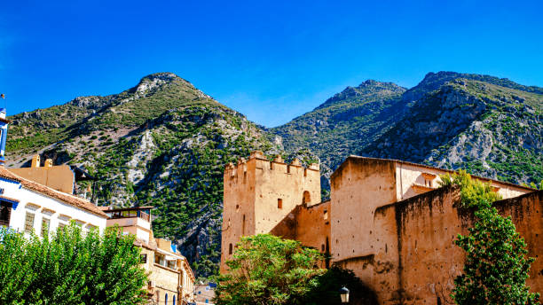 A historic kasbah in Chefchaouen, Morocco, with ochre walls contrasting lush green mountains, under a bright blue sky that enhances the site's unique beauty and authentic charm.