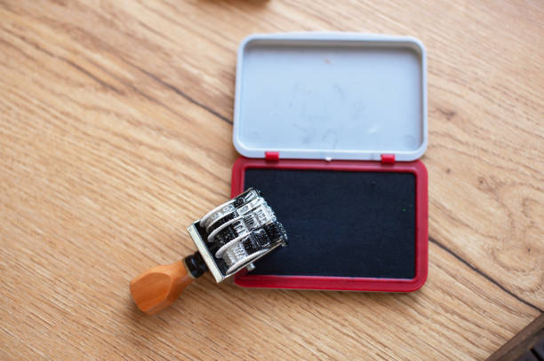 A classic office date stamp next to its accompanying red ink pad, lying open on a wooden desktop