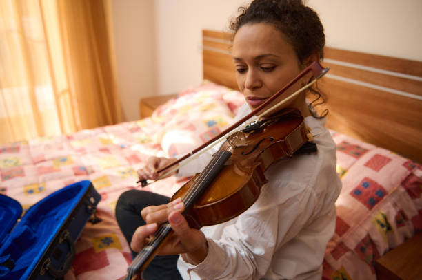 istock Woman practicing violin on her bed surrounded by warm sunlight 2187897997
