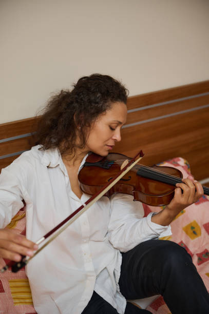 istock Woman in white shirt playing violin at home with focused expression 2187898018