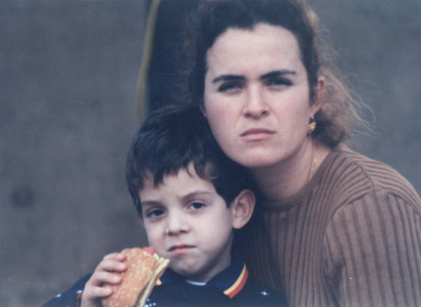 snímek pořízený v roce 1980: seriózní mladá žena pózuje se svým synem, který drží bagetový sendvič a dívá se do kamery - 1985 fotky - stock snímky, obrázky a fotky