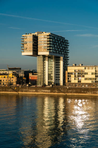 istock Modern riverside building with a unique architectural design reflects on the calm water under a clear blue sky. The warm sunlight highlights its structure and nearby surroundings. Landscape of Cologne 2187906388