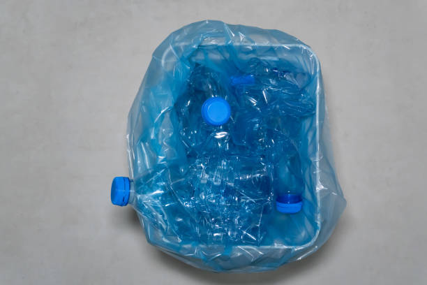 istock Plastic waste: A trash bin with crumpled plastic water bottles with blue caps sticking out. 2187907436
