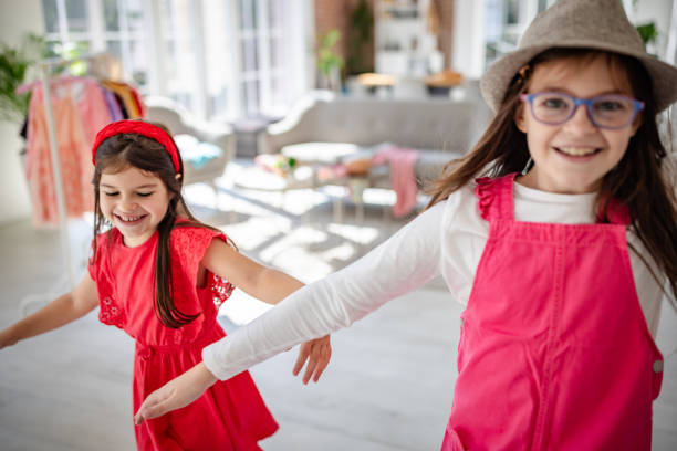 Two young girls energetically dance in vibrant red dresses within a stylish, sunny interior, exuding a lively and carefree spirit in the heart of a bright home.