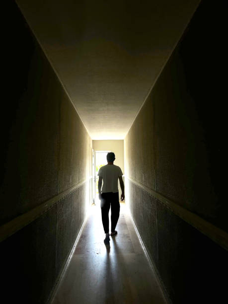 istock Single man walking at dark narrow corridor towards glowing door 2187914656