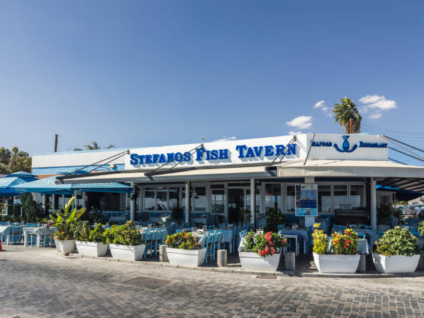 The bright and inviting facade of Stefanos Fish Tavern, showcasing blue-themed outdoor seating and vibrant flower pots, is located in a sunny coastal area. Larnaca, Cyprus - October 23, 2024.