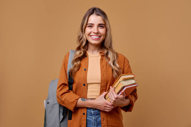 istock A Smiling Student is Holding a Stack of Books in Front of a Warm and Inviting Background 2187915104