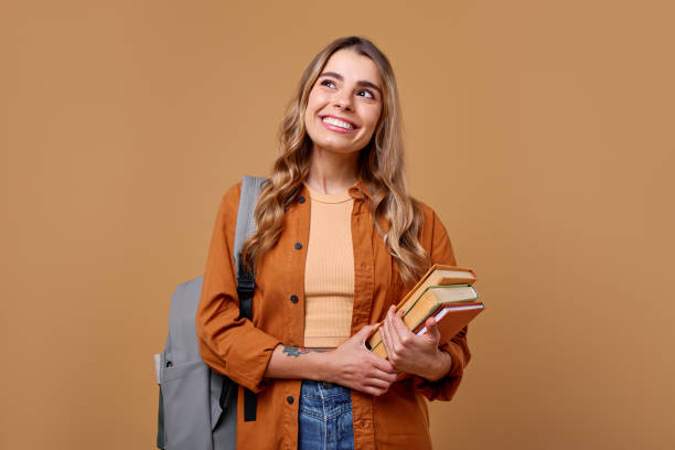 istock A Smiling Student is Holding a Stack of Books in Front of a Warm and Inviting Background 2187915112