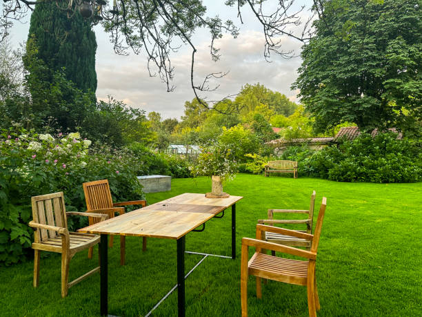 istock Evening garden scene with wooden chairs and a table set under a large tree 2187915475
