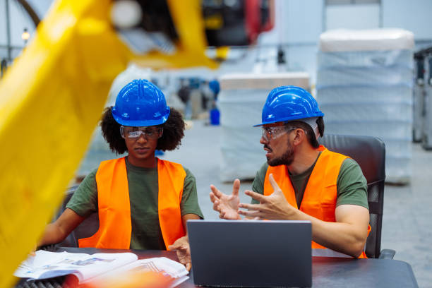 istock Engineers discussing using laptop in factory with robotic arm 2187918312