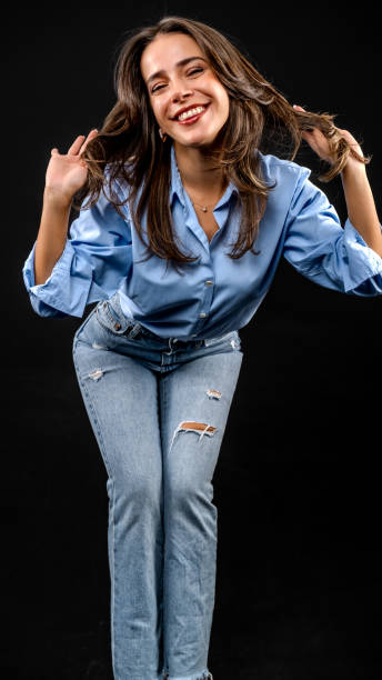 istock In a studio setting with a black background, a young brown-haired woman wearing a blue shirt and jeans is posing in an artistic style 2187920564