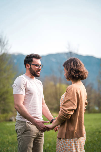 Hispanic mid adult male and Caucasian female enjoy a leisurely walk, holding hands amid the greenery of a hotel's serene garden.