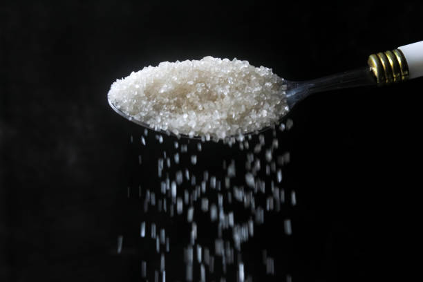 a spoon pouring granulated sugar, on a black background