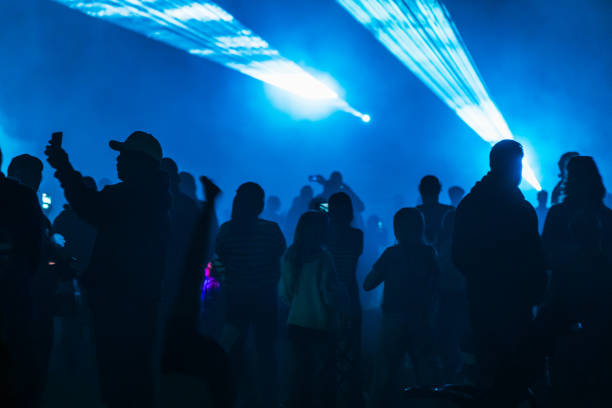Silhouettes of people in an illuminated blue lighting in concert hall enjoying rock music in lively atmosphere.