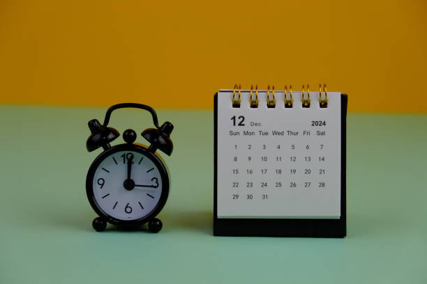 istock Monthly desk calendar for end and new year on wooden table with black alarm clock. 2187947708