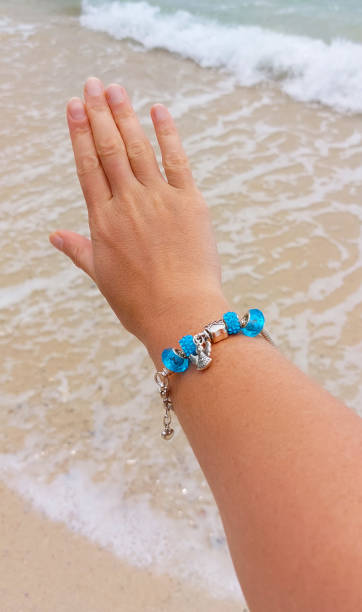 istock Woman's hand with charm bracelet extends towards calming ocean waves lapping on a sandy shore 2187948779