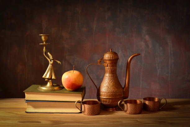 Still life, copper jug, coffee cups, books, figure and apple on the table