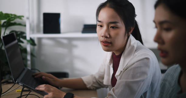 istock Asian female software developer explaining work to her colleagues at desk in an office. 2187976859