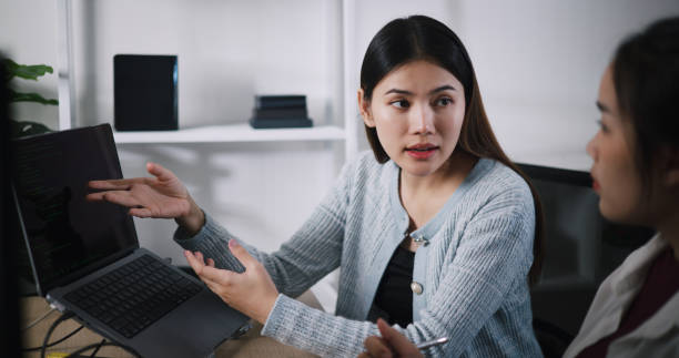 istock Asian female software developer explaining work to her colleagues at desk in an office. 2187976932