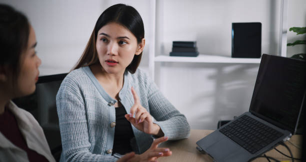 istock Asian female software developer explaining work to her colleagues at desk in an office. 2187976942