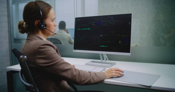 istock Female stock exchange trader talks on headset, monitors equity market and shares using computer 2187978247