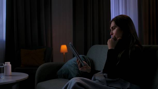 istock Woman suffering mental health issues, sitting on sofa covered in blanket, depressed expression, looks at tablet, smiling recalling memories, side view. 2187981187