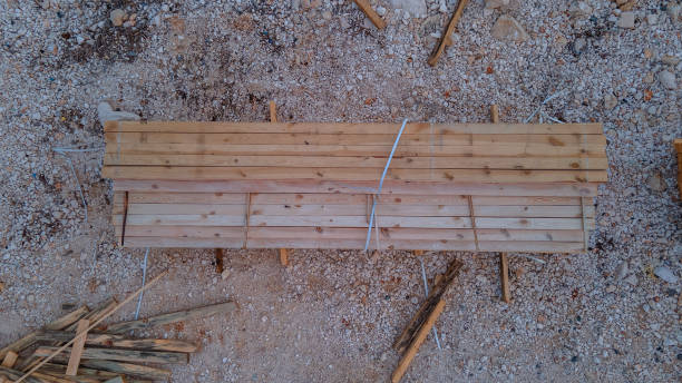 A top-down view of neatly arranged wooden beams at a construction site, showcasing organization and readiness for building projects under the warm sunlight