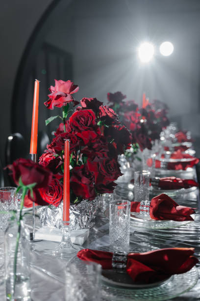 istock Festive table decorated with red roses, candles, napkins and served with silver tablecloth and dishes in a gray room 2187982841