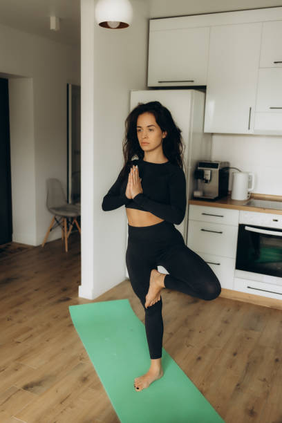 istock beautiful young woman doing yoga in the kitchen 2187989426
