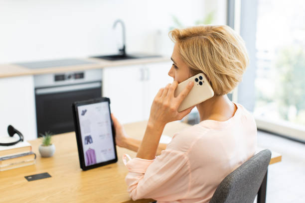 istock Caucasian woman shopping online using smartphone and tablet in modern kitchen 2187991891